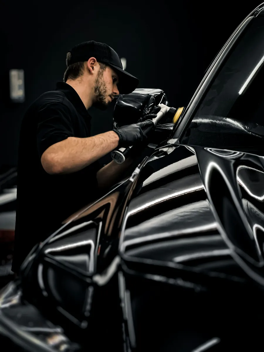 Detailer machine-polishing the front wing of a black car